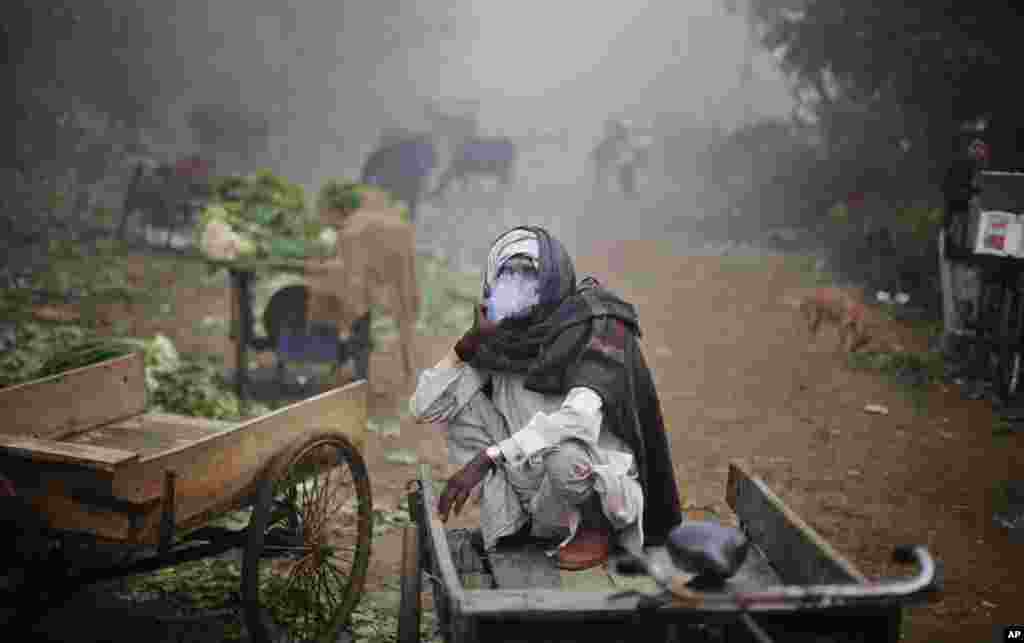 Seorang pekerja India merokok sambil duduk di becaknya di suatu pagi hari yang berkabut di New Delhi, India.