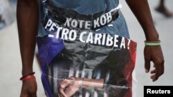 Yon nom kap mache nan manifestasyon ak yon postè ki ekri kot kòb Petro Caribe a e ki montre yon men ki minote dèyè bawo yon prizon. Pòtoprens, Ayiti, 10 septanm 2018. 