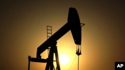 FILE - The sun sets behind an oil pump in the desert oil fields of Sakhir, Bahrain.