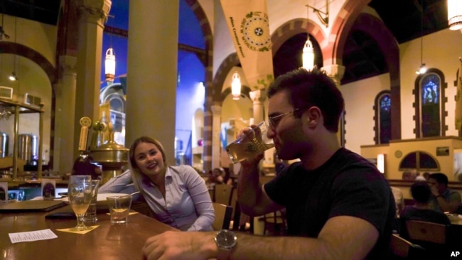FILE - Jesse Hulien, right, drinks a beer as Molly Hartman, left, looks on, at the Church Brew Works, a former church renovated into a brewery, in Pittsburgh, Aug. 7, 2017.