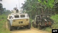 Un véhicule blindé de transport de troupes du contingent tanzanien de la MONUSCO, la Mission de l'Organisation des Nations Unies pour la stabilisation en République démocratique du Congo, passe devant une voiture de patrouille de l'UPDF (Forces de défense du peuple ougandais).