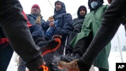 Migrants warm their feet by a fire at the Lipa camp northwestern Bosnia, near the border with Croatia, Dec. 26, 2020. 