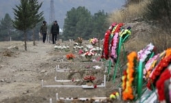 FILE - Men walk along graves of soldiers and civilians who were killed during a military conflict over the breakaway region of Nagorno-Karabakh, in Stepanakert, Nov. 2, 2020.