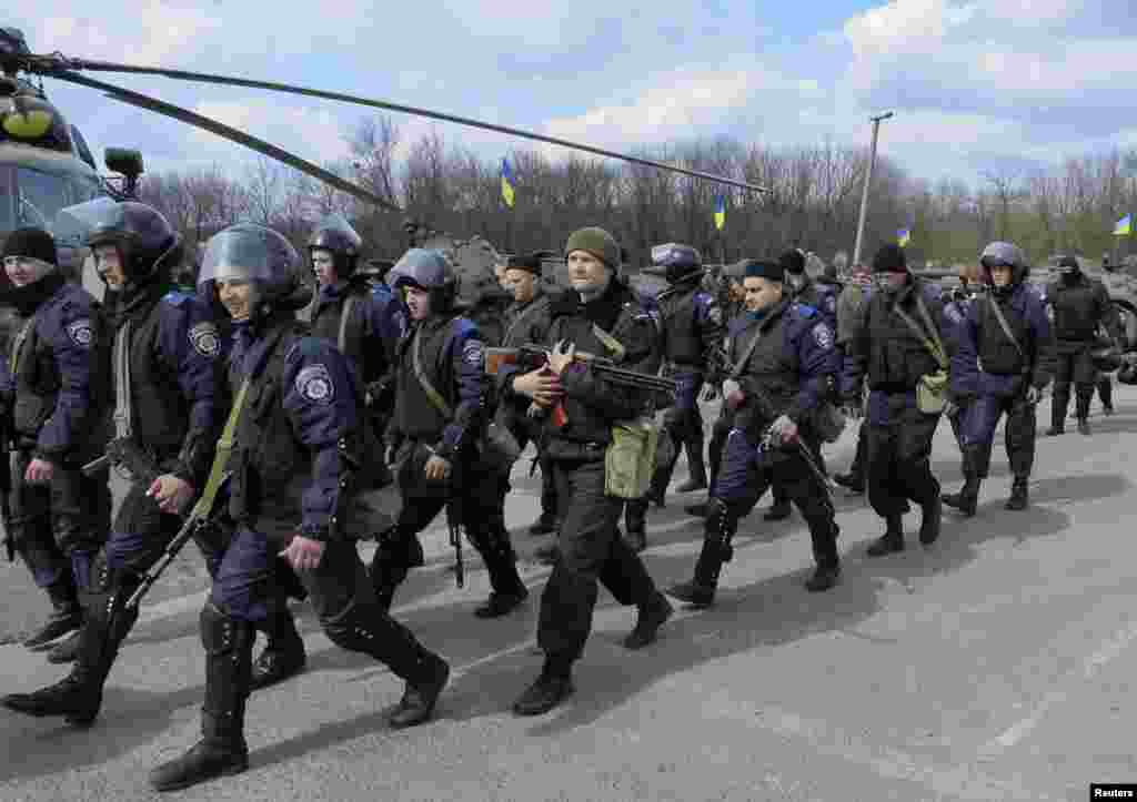 Members of the Ukrainian Interior Ministry walk past an MI-8 military helicopter and armored personnel carriers at a checkpoint near the town of Izyum, eastern Ukraine, April 15, 2014.