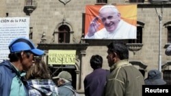 FILE - Pedestrians walk at San Francisco square where an image of Pope Francis is displayed in La Paz, Bolivia, June 30, 2015. 