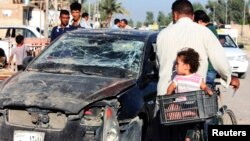 Residents pass by a damaged vehicle a day after a bomb attack in central Baquba, 65 km northeast of Baghdad, Aug. 25, 2013.