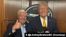 سناتور گراهام در کنار دونالد ترامپ، رئیس جمهوری آمریکا که کلاه «ایران را دوباره با عظمت کن» در دست گرتفه است