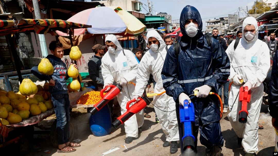 Workers wearing protective gear spray disinfectant as a precaution against the coronavirus, at the main market in Gaza City, March 19, 2020.