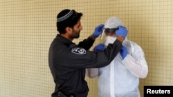An Israeli police officer helps a Health Ministry inspector put on protective gear before they go up to the apartment of a person in self-quarantine as a precaution against the coronavirus spread, in Hadera, Israel, March 16, 2020.