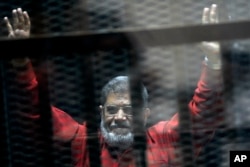 FILE - In this June 21, 2015 file photo, former Egyptian President Mohammed Morsi, wearing a red jumpsuit that designates he has been sentenced to death, raises his hands inside a defendants cage