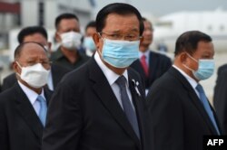 FILE - Prime Minister Hun Sen, center, wears a face mask as a preventive measure against the spread of the COVID-19 novel coronavirus, at Phnom Penh International Airport, May 11, 2020.