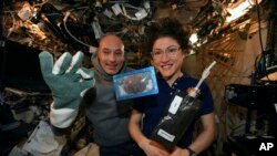 In this photo made available by U.S. astronaut Christina Koch via Twitter on Dec. 26, 2019, she and Italian astronaut Luca Parmitano pose for a photo with a cookie baked on the International Space Station.