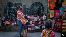 A child hugs her mother as a sibling watches at their sidewalk shop aimed for tourists in Bangkok, Thailand, Wednesday, July 29, 2020. Thailand has been effective in controlling COVID-19 infections over the last three months, but its economy is…