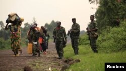 Displaced families walk past M23 rebels at Rumangabo, after government troops abandoned the town 23 km (14 miles) north of the eastern Congolese city of Goma, July 28, 2012. 