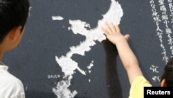 A Okinawa boy touches the map of Okinawa carved on a stone face near the U.S. Marine Corps Air Station Futenma in Ginowan. (File)