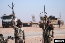 FILE - Syrian Democratic Forces (SDF) fighters hold up their weapons in the north of Raqqa city, Syria.