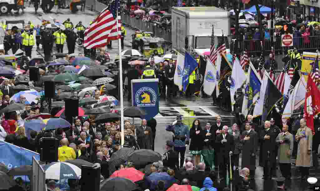 Sobreviventes, familiares das vítimas, autoridades, equipas de emergência e convidados param enquanto a bandiera dos Estados Unidos é içada na meta da maratona de Boston, num tributo às vítimas do ataque bombista do ano passado, Abril 15, 2014.