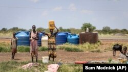 In this photo taken Monday, Oct. 1, 2018, residents stand by the side of the road after fetching water, between Melut and Paloch town, in South Sudan.