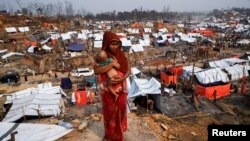 Seorang perempuan pengungsi Rohingya menggendong anaknya di tengah kamp pengungsi Cox's Bazar, Bangladesh, yang terdampak kebakaran besar dua hari lalu, 24 Maret 2021. (REUTERS / Mohammad Ponir Hossain)