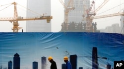 FILE - Workers walk past a billboard display showing a scene of Central Business District, as capital city skylines are shrouded with pollutant haze in Beijing, China, Nov. 9, 2015. 