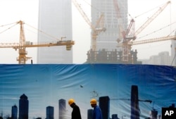 FILE - Workers walk past a billboard display showing a scene of Central Business District, as capital city skylines are shrouded with pollutant haze in Beijing, China, Nov. 9, 2015.