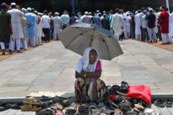 Seorang perempuan duduk di bawah naungan payung dan mengawasi alas kaki para jemaah yang datang untuk salat Jumat terakhir di bulan suci Ramadan, di Masjid Mekah, Hyderabad, India, Jumat, 7 Mei 2021. (AP)