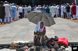 Seorang perempuan duduk di bawah naungan payung dan mengawasi alas kaki para jemaah yang datang untuk salat Jumat terakhir di bulan suci Ramadan, di Masjid Mekah, Hyderabad, India, Jumat, 7 Mei 2021. (AP)
