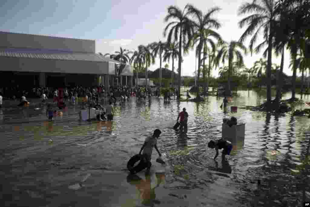 People wade through waist-high water in a store's parking, looking for valuables, south of Acapulco, in Punta Diamante, Mexico, Sept. 18, 2013. 