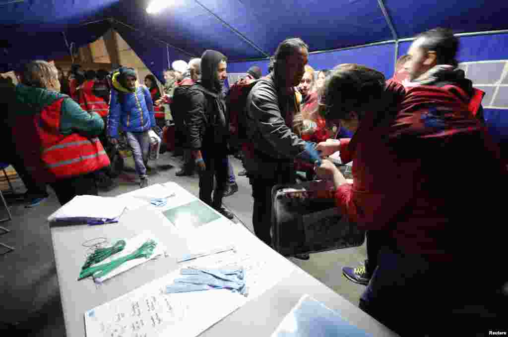 Para migran mendapat gelang berwarna pusat pemrosesan pada hari kedua evakuasi dan pemindahan mereka dari kamp Calais (25/10). (Reuters/Philippe Wojazer)