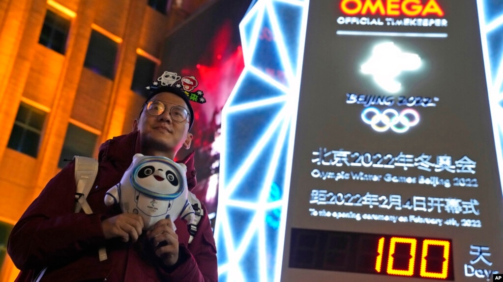 A supporter of the 2022 Beijing Winter Olympics poses for photos with a countdown clock as it crosses into the 100 days countdown to the opening of the Winter Olympics in Beijing, China, Oct. 26, 2021.