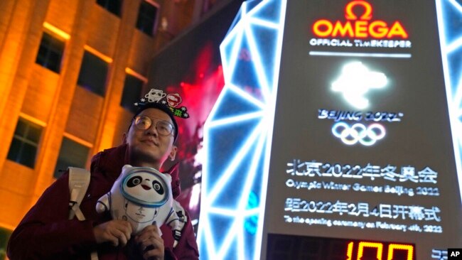 A supporter of the 2022 Beijing Winter Olympics poses for photos with a countdown clock as it crosses into the 100 days countdown to the opening of the Winter Olympics in Beijing, China, Oct. 26, 2021.