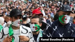 Des manifestants se couvrent le visage avec des drapeaux nationaux lors d'une manifestation anti-gouvernementale à Alger, Algérie, le 13 mars 2020. 