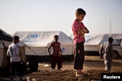 A boy, who fled from the violence in Mosul, stands near tents in a camp for internally displaced people on the outskirts of Arbil in Iraq's Kurdistan region, June 14, 2014.
