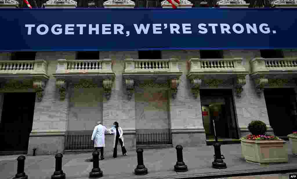 Medical workers touch elbows to greet each other as they arrive before the opening bell at the New York Stock Exchange in New York City. The NYSE opened to in-person activity for the first time in two months.