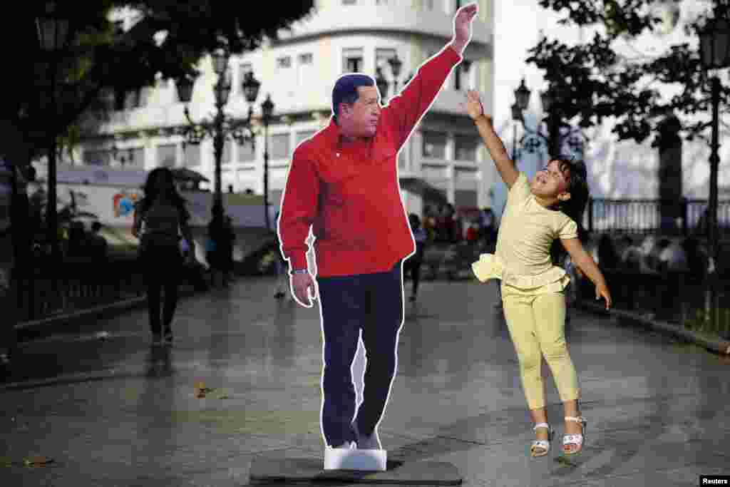 A girl jumps next to a picture of late Venezuela&#39;s president Hugo Chavez at Plaza Bolivar in Caracas. Followers of Chavez are commemorating the first anniversary of his death this week, March 9, 2014.