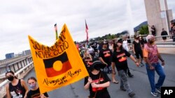 Para pengunjuk rasa memegang plakat saat berpawai dalam aksi protes menandai peringatan 50 tahun Kedutaan Besar Aborigin, di Canberra, Rabu, 26 Januari 2022. (Lukas Coch/AAP Image via AP)