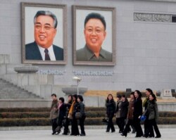 FILE - North Korean women walk in front of portraits of North Korea's founder Kim Il-sung (L) and late leader Kim Jong-il at Kim Il-sung Square in Pyongyang, in this photo provided by Kyodo, April 1, 2013.