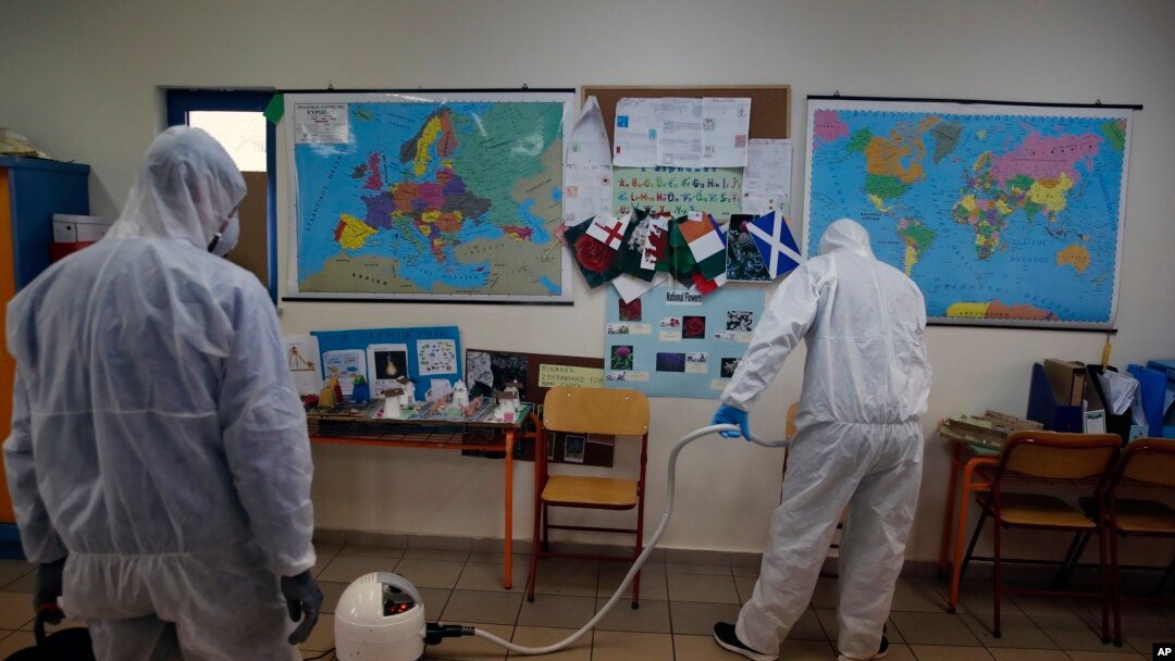 Workers wearing protective suits spray disinfectant inside a classroom at a primary school in Athens, March 9, 2020. 
