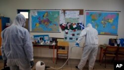 Workers wearing protective suits spray disinfectant inside a classroom at a primary school in Athens, March 9, 2020. 
