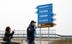 A police officer discusses with a woman as he checks transit to and from the cordoned area in Guardamiglio, Italy, Feb. 25, 2020.