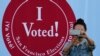 Foto de mulher em frente a sinal "Eu votei" em centro eleitoral em São Francisco 