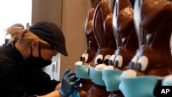An employee at a cake shop prepares chocolate Easter bunnies with masks, in Lykovrisi, northern Athens, Greece.