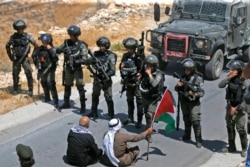 Pengunjuk rasa Palestina duduk di depan pasukan Israel selama demonstrasi menentang perampasan tanah Palestina oleh Israel, di desa Kafr Malik timur laut Ramallah di Tepi Barat yang diduduki Israel, 16 Agustus 2019. (Foto: AFP)