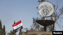 FILE - A Syrian national flag flutters next to the Islamic State's slogan at a roundabout where executions were carried out by IS militants in the city of Palmyra, in Homs Governorate, Syria, April 1, 2016.