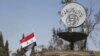 FILE - A Syrian national flag flutters next to the Islamic State's slogan at a roundabout where executions were carried out by IS militants in the city of Palmyra, in Homs Governorate, Syria, April 1, 2016.