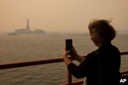 A person takes a picture of the Statue of Liberty, covered in a haze-filled sky, from Staten Island Ferry, Wednesday, June 7, 2023, in New York.