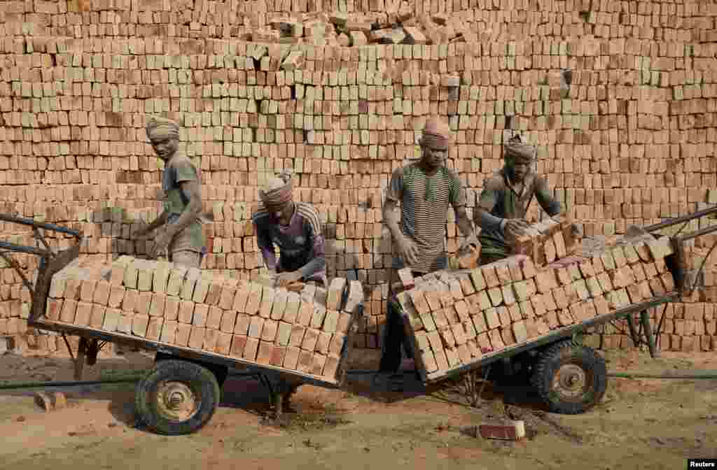 Workers at a brick factory stack bricks on carts in Dhaka, Bangladesh.