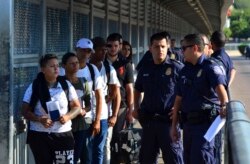 FILE - U.S. Customs and Border Patrol officials wait to hand asylum-seekers over to Mexican officials as they are returned under the so-called 'Remain in Mexico' program, between Laredo, Texas, and Nuevo Laredo, Mexico, July 10, 2019.