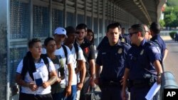 FILE - U.S. Customs and Border Patrol officers are seen with asylum-seekers on the international bridge between Laredo, Texas, and Nuevo Laredo, Mexico, July 10, 2019.