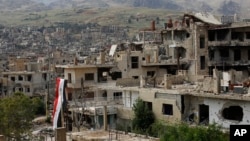 FILE - A Syrian national flag hangs from a damaged building in the town of Zabadani in southwestern Syria, May 18, 2017. Syrian government troops have been regaining territory in the country's southwestern regions which fell to anti-regime rebels in the early years of the conflict.